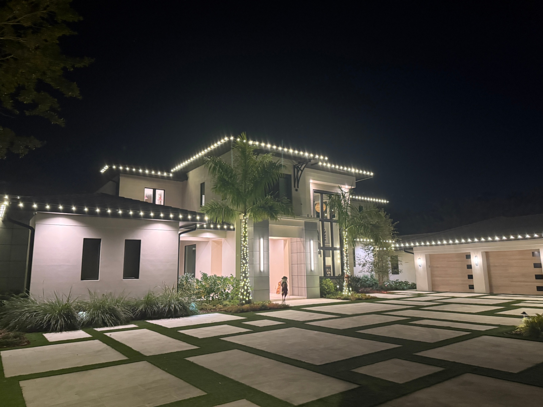 Modern home highlighted by warm white holiday roofline lighting and palm wraps