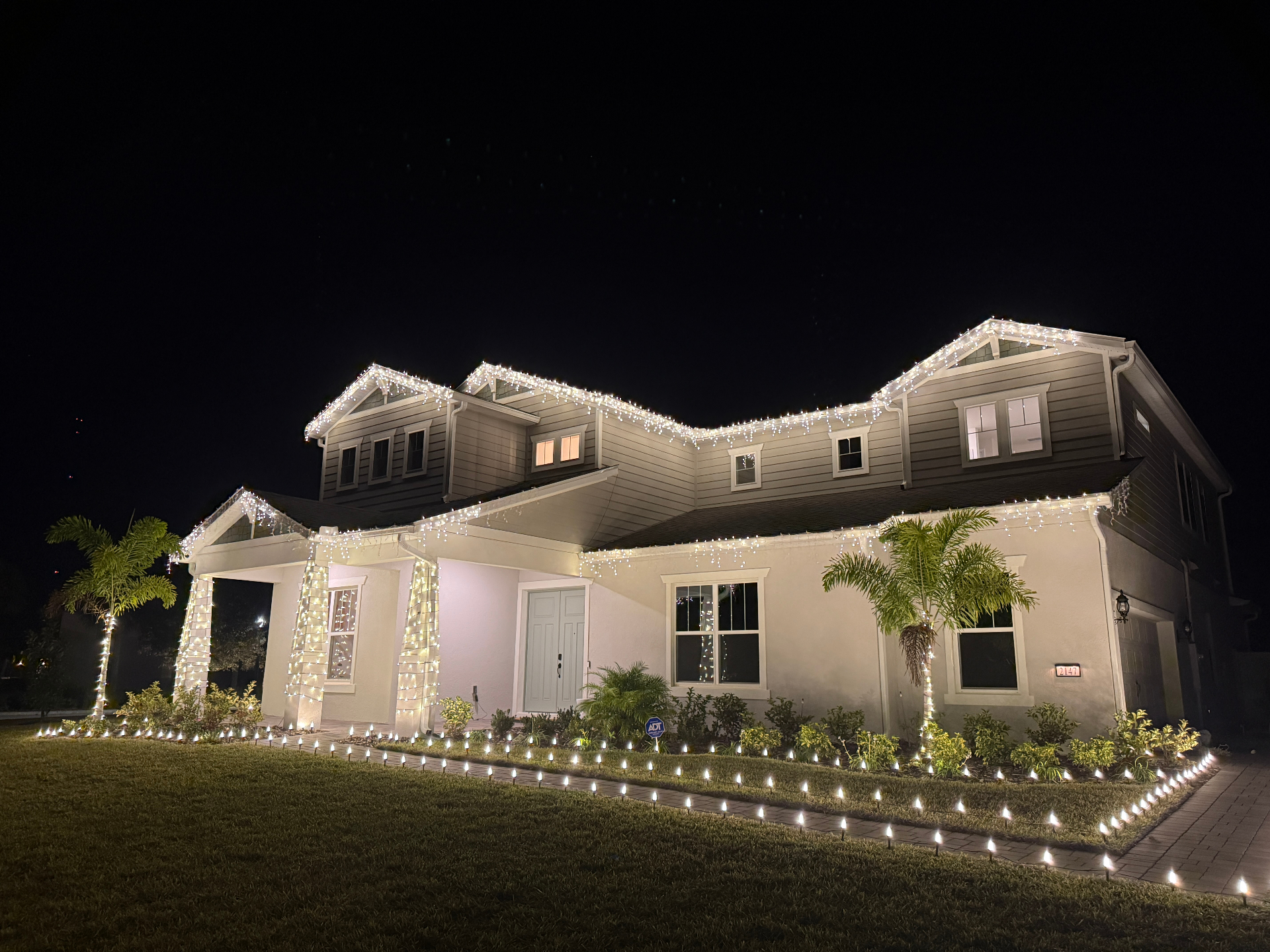 Two-story home decorated with icicle roofline lights and glowing pathway accents