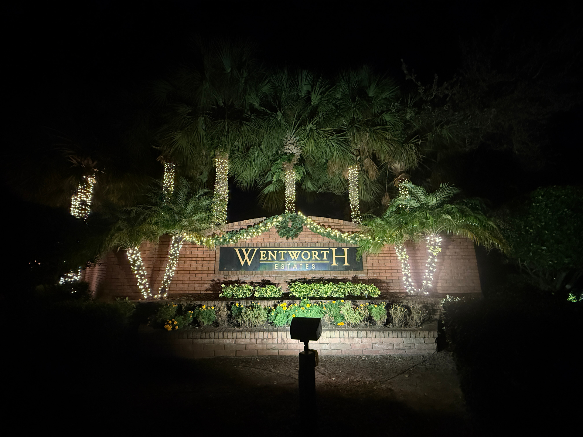 Community entrance sign decorated with garland and wrapped palm trees for the holidays