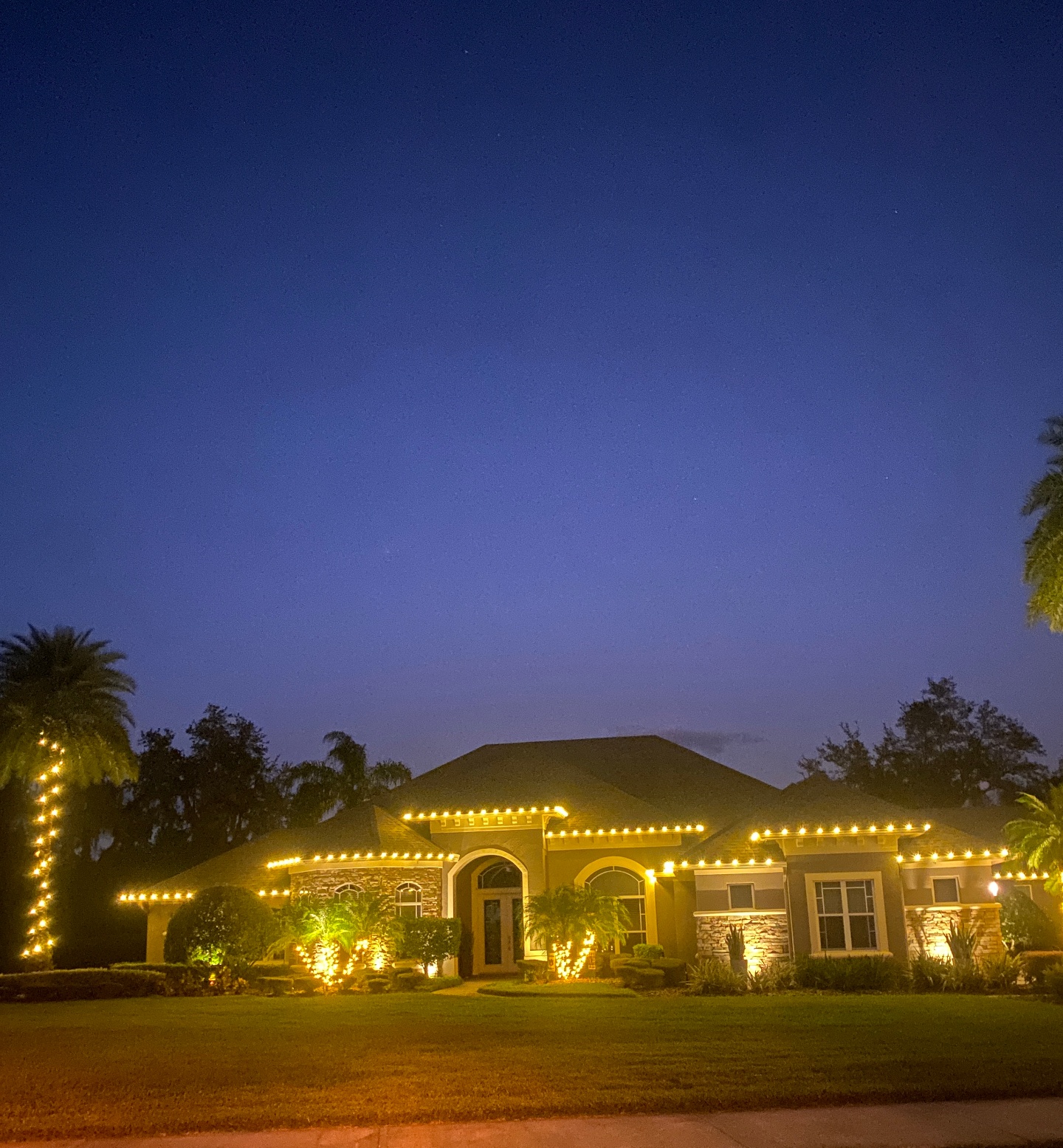 Estate home at twilight with warm C9 roofline holiday lighting