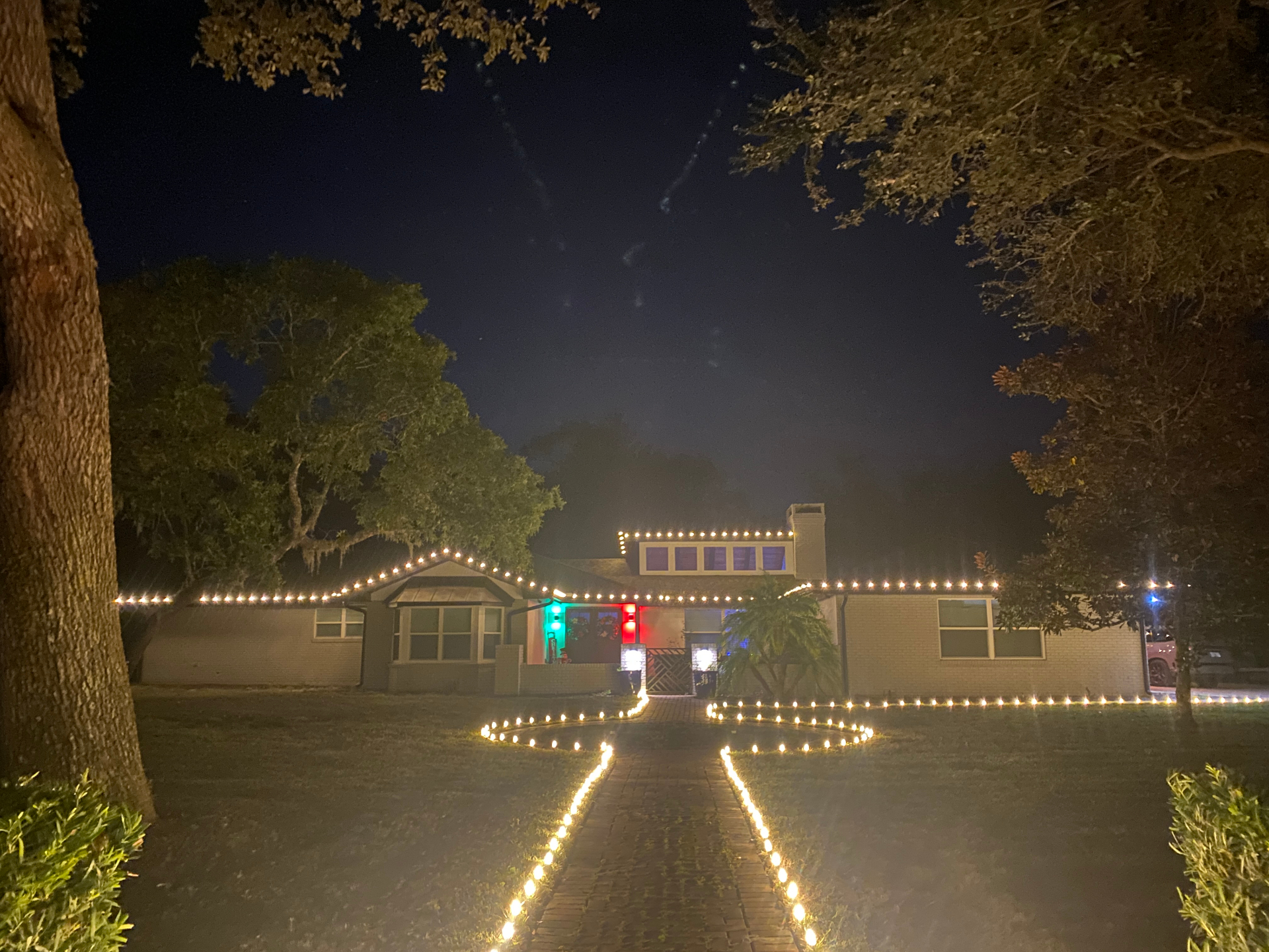 Ranch home with warm white roofline lights and a lit swirl pathway to the front door
