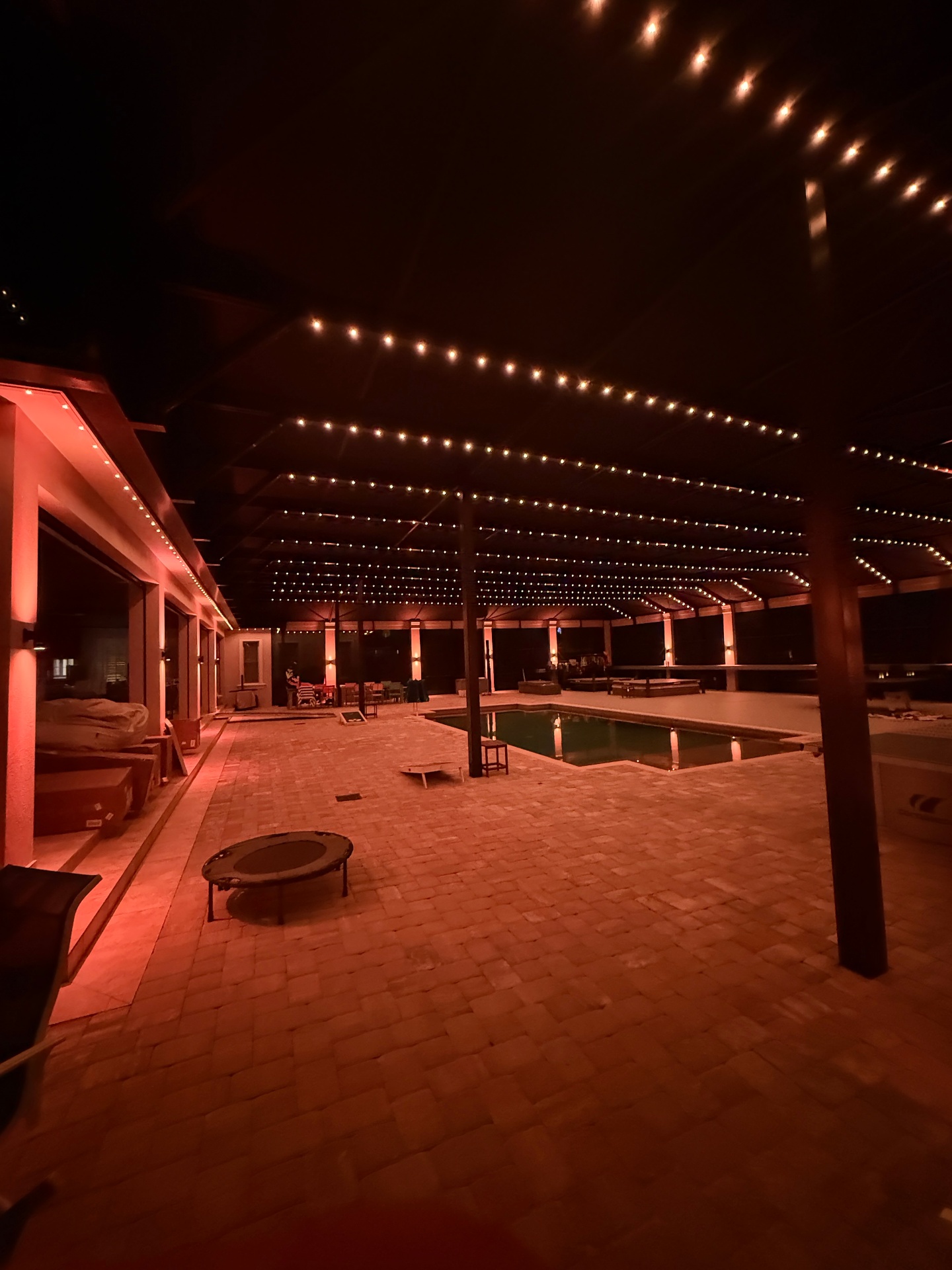 Covered pool deck with warm bistro-style permanent lighting across the lanai ceiling
