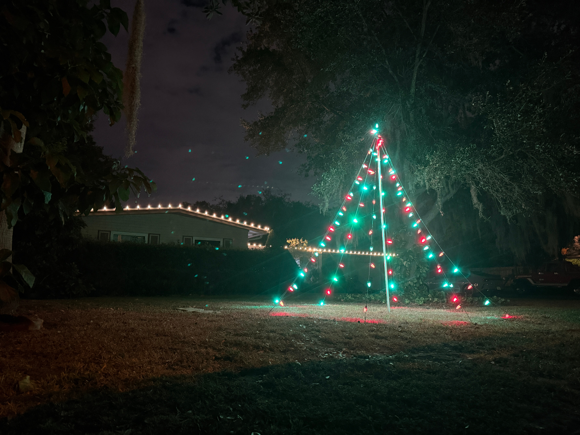 Large outdoor Christmas light tree display beside a home with roofline lighting